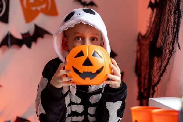 Niño de Halloween con cubos de caramelo de calabaza en traje de esqueleto en casa. Listo para engañar o tratar vacaciones —  Fotos de Stock