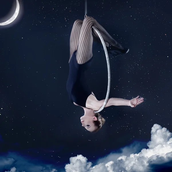 Женщина висит вверх ногами на воздушном обруче ночью — стоковое фото