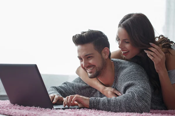Happy couple prone on carpet online shopping — Stock Photo, Image