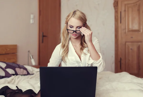 Sexy blonde vrouw op bed online chatten door laptop — Stockfoto