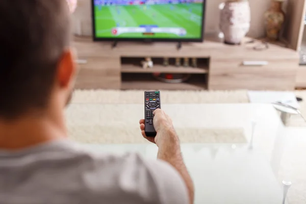 Man with remote control watching football match