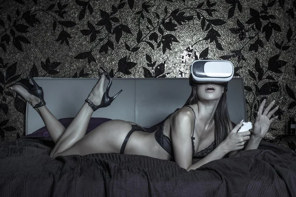 Sexy giovane donna utilizzando VR auricolare e telecomando a letto — Foto Stock