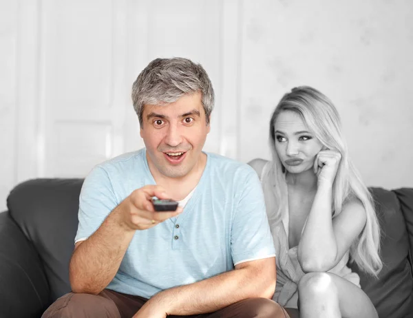 Man switching TV channel on remote control boring wife