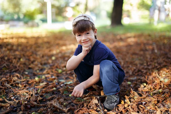 Mały chłopiec z czapkę kucać w przyrodzie — Zdjęcie stockowe