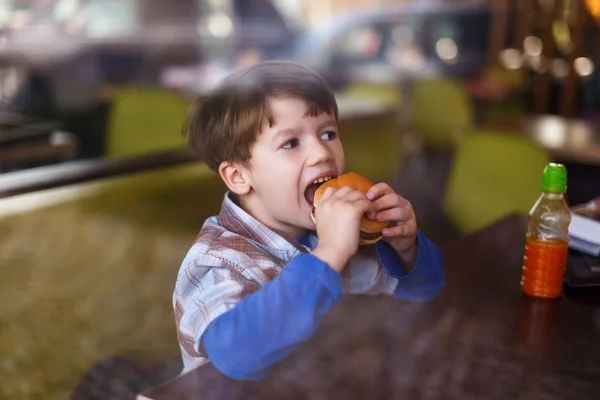 Niño comiendo hamburguesa en restaurante de comida rápida — Foto de Stock