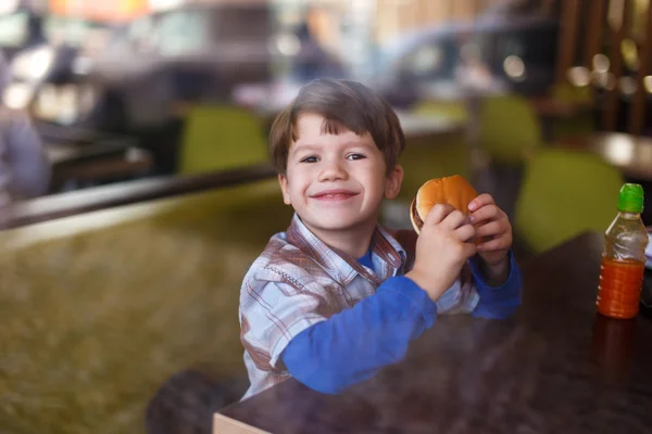 Petit garçon sourire avec hamburger au restaurant fast food — Photo