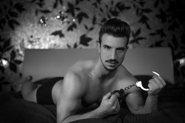 Sexy macho hombre con esposas en la cama en blanco y negro —  Fotos de Stock