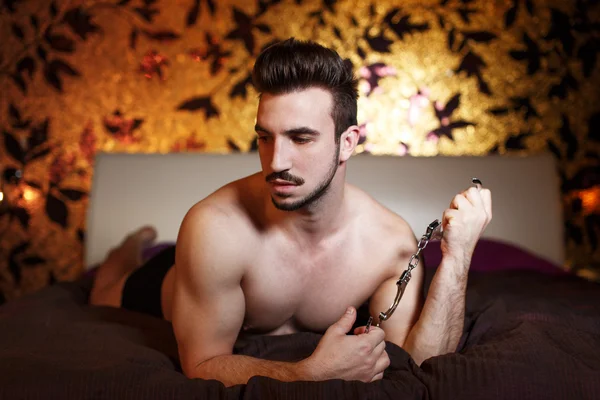 Sexy macho hombre sosteniendo esposas en la cama —  Fotos de Stock