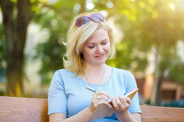 Blondine schreibt ins Notizbuch — Stockfoto