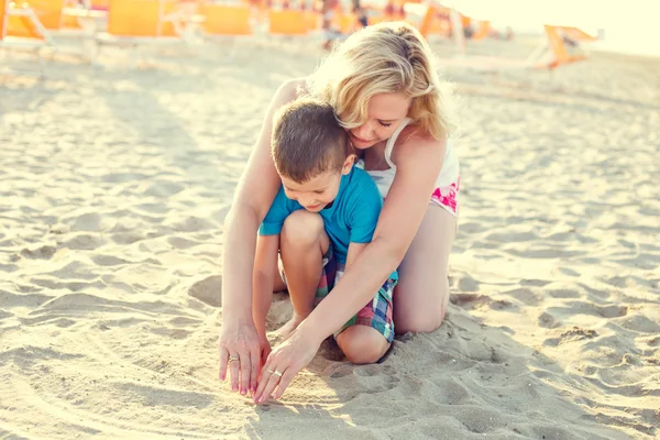 Happy little boy with mother drawing heart into sand — Stock Photo, Image