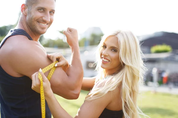 Blonde woman measure mans biceps by yellow measuring tape — Stock Photo, Image