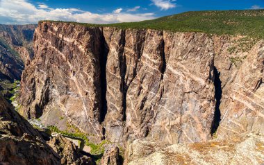 Gunnison Ulusal Parkı 'nın Kara Kanyon' undaki devasa Boyalı Duvar manzarası. Beyaz pegmatit çukurları karanlıkta çizgiler oluşturur, dik uçurum. Gunnison Nehri aşağıda görünüyor.