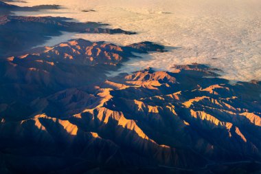 Peru 'daki And Dağları' nın havadan görünüşü. Altın gün doğumu ışığı yüksek tepeleri aydınlatırken derin vadiler ve bir bulut denizi gölgede.