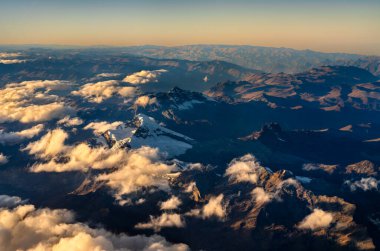 Peru 'daki And Dağları' nın havadan görünüşü. Altın gün doğumu ışığı yüksek tepeleri aydınlatırken derin vadiler ve bir bulut denizi gölgede.