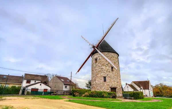 Tarihi Moulin de Montfermeil ya da Sempin Windmill, Fransa. Tahta bıçaklı taş yapı bulutlu bir gökyüzünün altındaki evlerle çevrili bir parkta duruyor.