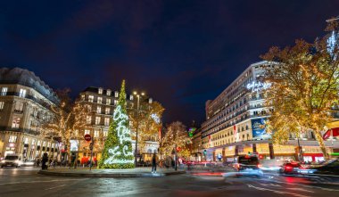 Paris, Fransa - 8 Aralık 2025: Haussmann Bulvarı 'ndaki Galeries Lafayette yakınlarındaki Place Diaghilev' de aydınlatılmış Noel ağacı duruyor. Şenlikli tatil kurulumunda gece gökyüzünün altında neon ışıklar yer almaktadır