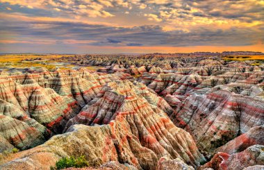 Badlands Overlook, Güney Dakota, ABD 'deki Badlands Ulusal Parkı' nda yer alıyor. Manzarada rengarenk aşınmış kaya oluşumları ve bulutlu bir günbatımı gökyüzünün altında tortul katmanlar yer alır.