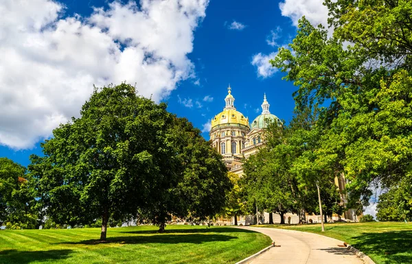 Des Moines 'teki Iowa Eyalet Meclisi. Tarihi mimaride merkezi altın kubbe ve daha küçük bakır kubbeler mavi gökyüzünün altındaki yeşil ağaçların arasından görülür.