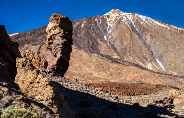 Teide Ulusal Parkı, Tenerife, Kanarya Adaları 'ndaki ünlü Roque Cinchado kaya oluşumu ve kar kaplı Teide Dağı volkanı manzarası. Manzara engebeli volkanik kayalara sahiptir..