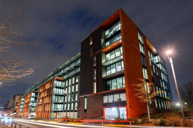 Saint Ouen, Fransa - 9 Aralık 2025: Paris yakınlarındaki trafik ışığı patikalı Alstom Genel Merkezi 'nin aydınlatılmış modern cam ve turuncu cephesi.