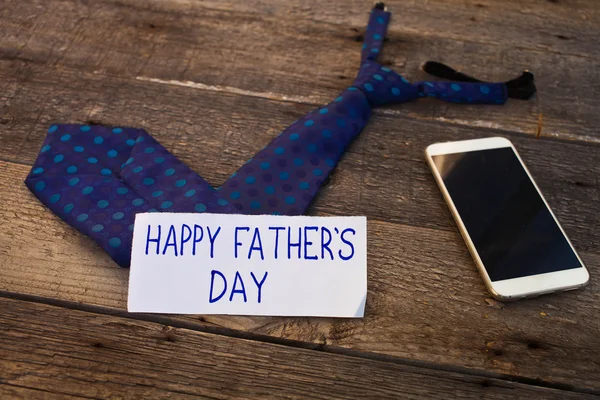 Happy Father's Day inscription with mobile phone and tie on wood