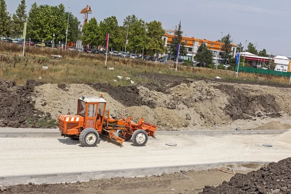 Grader laranja está nivelando o chão de cascalho no local de construção . — Fotografia de Stock