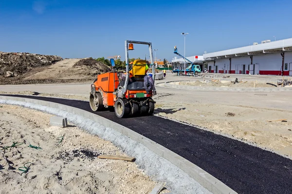 Pequeña apisonadora es flatting largo camino nuevo hecho de asfalto . —  Fotos de Stock