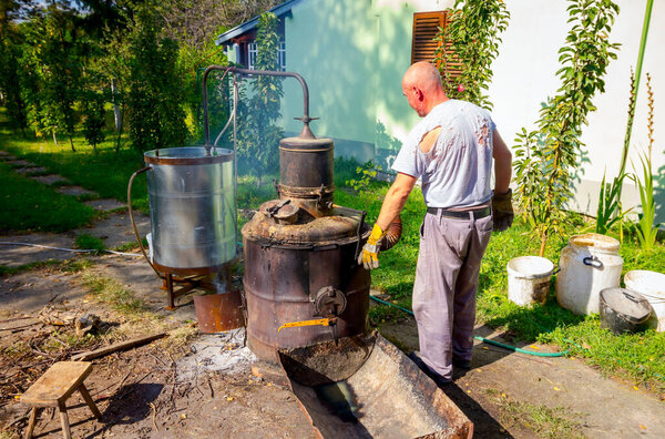 Человек вручную поворачивает рычаг, чтобы смешать фруктовый марк в котле самодельного ликеро-водочного завода из меди, делая самогон шнапс, алкогольные напитки, такие как бренди, коньяк, виски, бурбон, джин, скотч.