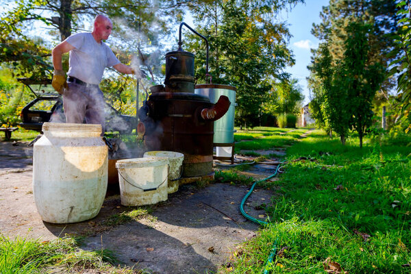 Человек разгружает котел самодельного ликеро-водочного завода из меди для выпуска подержанных фруктов марки, делая самогон шнапс, алкогольные напитки, такие как бренди, коньяк, виски, бурбон, джин и скотч.