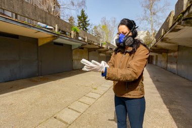 Yüzünde filtre maskesi olan kadın COVID-19 virüsüne karşı korunmak için ellerine lastik eldiven takıyor.. 