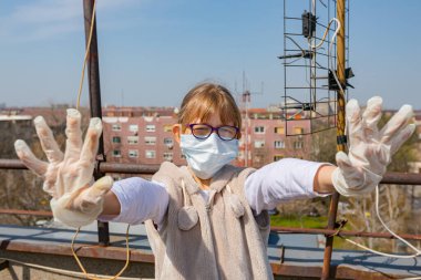 Medya baskısını durdurun. Tıbbi maske takan ve eldiven takan küçük kız ellerini, jestlerini, sosyal mesafelerini, uzak durduğunu, COVID-19 virüsüne karşı korunduğunu gösteriyor..