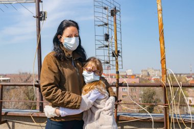 Medya baskısını durdurun. Anne, korkmuş kızını kucaklıyor. Eldivenleri ve maskeleri var. COVID-19 virüsünden korunmak için..