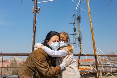 Medya baskısını durdurun. Anne, korkmuş kızını kucaklıyor. Eldivenleri ve maskeleri var. COVID-19 virüsünden korunmak için..