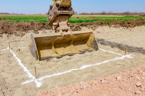 Excavator will excavate square trench that is marked with white powder lime at construction site, project in progress.