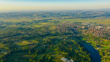 Yeşil tepenin üzerinde gölle çekilmiş, uzaktaki orman ağaçları ve şehirler arasında ekilmiş araziler..