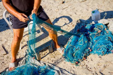 Balıkçı kumlu sahilde balık ağı biriktirir ve bir sonraki oltaya hazırlanır.. 