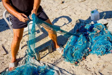 Fisherman pile up fishnet on the sandy beach and prepare for his next angling.  clipart
