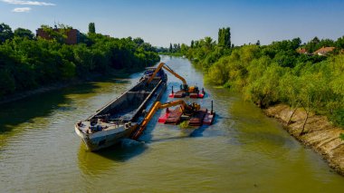 Nehir, kanal, derinleşen ve kirli bir su yolundaki tortu ve çamuru nehir yatağından kaldıran iki kazıcının üzerini tararken, tararken, tararken, tararken, tararken ve temizlerken.