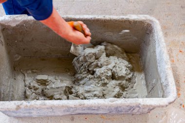 İşçi sığ plastik kaplarda harç yakalamak için spatula kullanıyor..