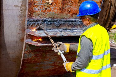 İşçi, oksijen, asetilen ve propan karışımı kullanarak elle eski metal yapısını kesiyor..