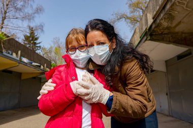 Anne, korkmuş kızını kucaklıyor. Eldivenleri ve maskeleri var. COVID-19 virüsünden korunmak için..