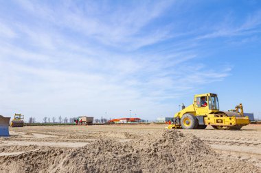Titreşim plaka sıkıştırıcı buharlı silindire monte edilir ve yol inşaatında kum sıkıştırılır..