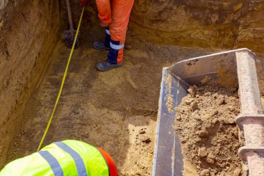 İşçiler, metrekarelik siperlerdeki ölçümleri kontrol etmek için metal mezura ve metre kullanıyorlar..