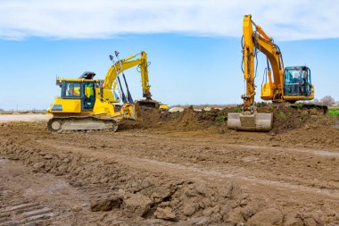 İki kazıcı ve buldozer toprağı dümdüz ediyor, bu da inşaat alanını eşitliyor..