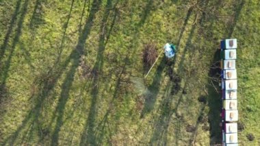 Koruyucu giysiler içindeki çiftçinin hava manzarası meyve ağaçlarını mantar hastalıklarından veya parazitlerden korumak için uzun spreyler kullanıyor. Arı kolonisi yakınlarında, arı kolonisi yakınlarında..