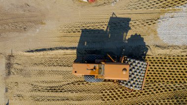 Tepede, tepede dikenli büyük bir yol silindiri var. Toprak sıkıştırıyor. İnşaat sahasında bir yol temeli var..