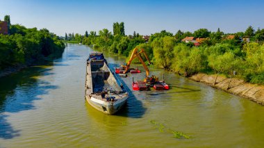 Nehir, kanal, derinleşen ve kirli bir su yolundaki tortu ve çamuru nehir yatağından kaldıran iki kazıcının üzerini tararken, tararken, tararken, tararken, tararken ve temizlerken.