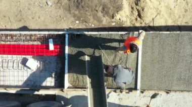 Üstten bakıldığında, inşaat işçisi tırmık ve küreği yaymak için kullanıyor, mikser kamyonundan dökülen taze betonu kare siperlere döküyor..