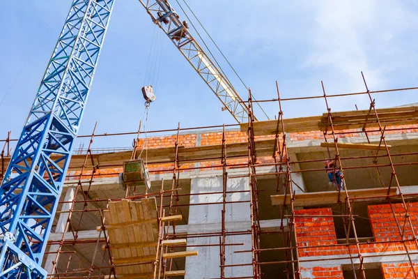 Workers are waiting crane to keep balance and direction to wheelbarrow, with mortar to placing on scaffold platform.