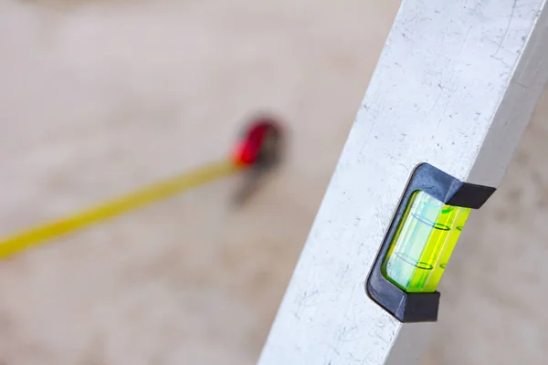 Spirit level placed next to the wall and metal measure tape is on the concrete floor after usage for construction site for measurement and control.